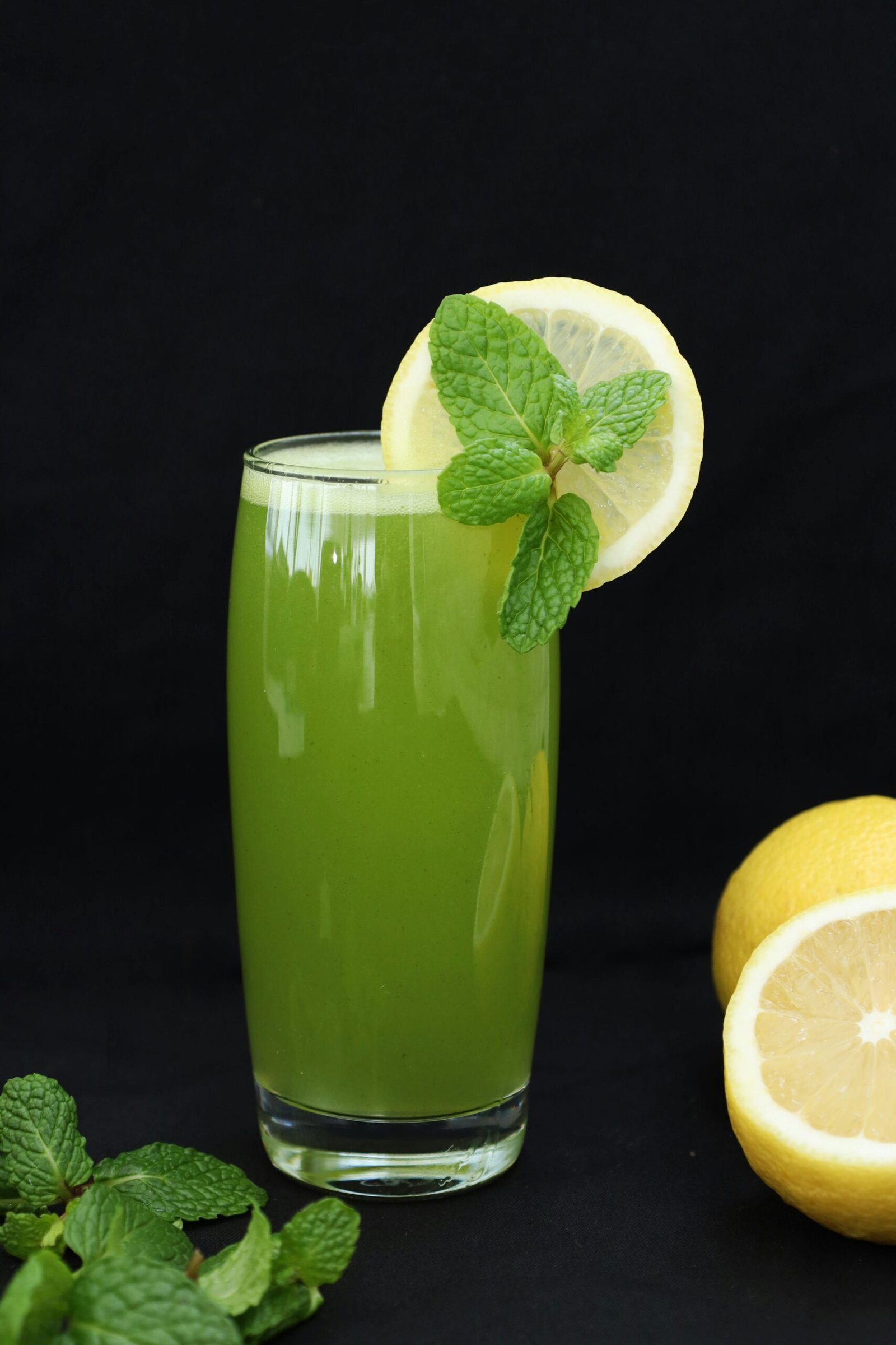 Vertical shot of a fresh mint lemonade glass garnished with lemon slice and mint leaves on black background.